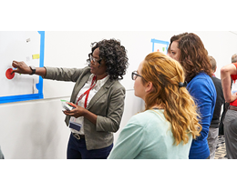 3 women looking at a white board. One is holding a red dot on the  board 