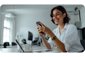 woman smiling and looking at her phone while sitting at a desk